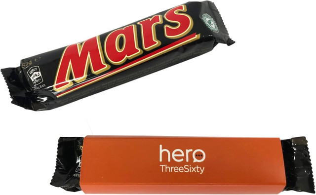 A Mars Bar wrapped in black packaging with an orange sleeve. The bar features a logo on the front.
