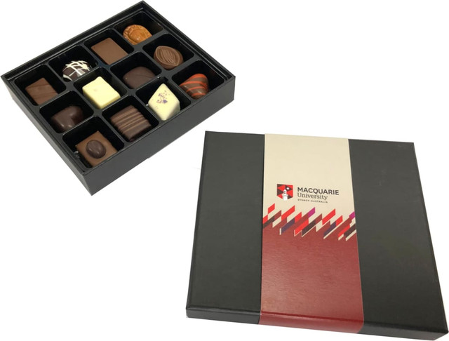 A black box containing an assortment of praline chocolates in various shapes and colours. The box has a logo.