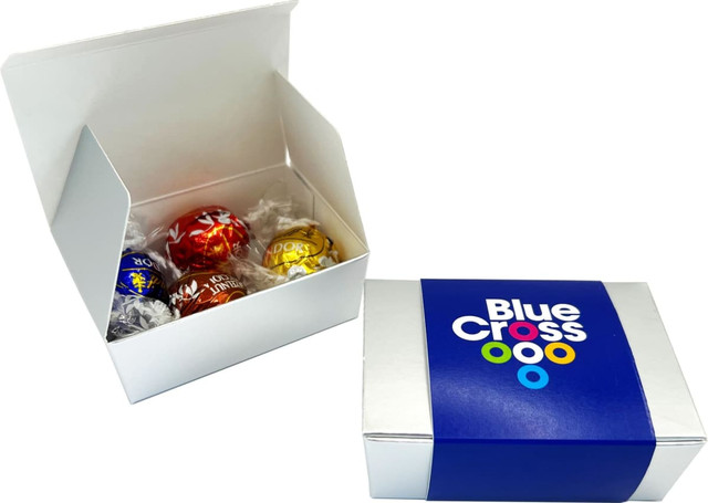 A white box containing four assorted chocolate balls, featuring vibrant red, yellow, and blue wrappers, with a branded outer sleeve.