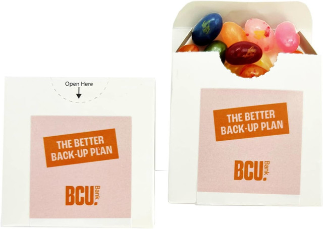 A flip lid cardboard box containing assorted JELLY BELLY jelly beans in various colours. It features a logo.