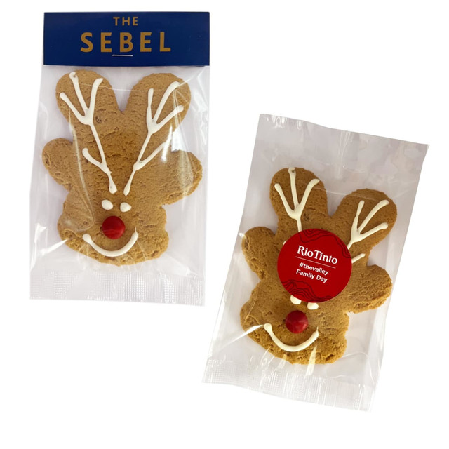 Gingerbread reindeer cookies in the shape of a reindeer, featuring white icing and a red candy nose, packaged in clear wrappers.