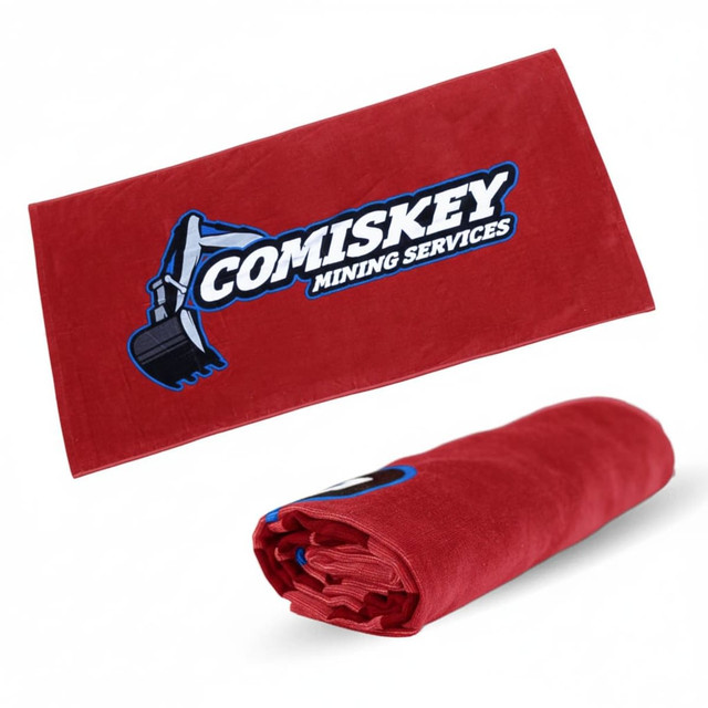 A rolled-up red beach towel with a logo featuring an excavator. The towel measures 75cm x 150cm.