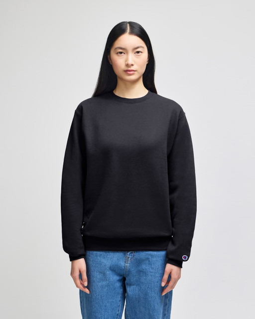 A black crewneck sweatshirt with long sleeves and a logo on one sleeve, displayed on a model.