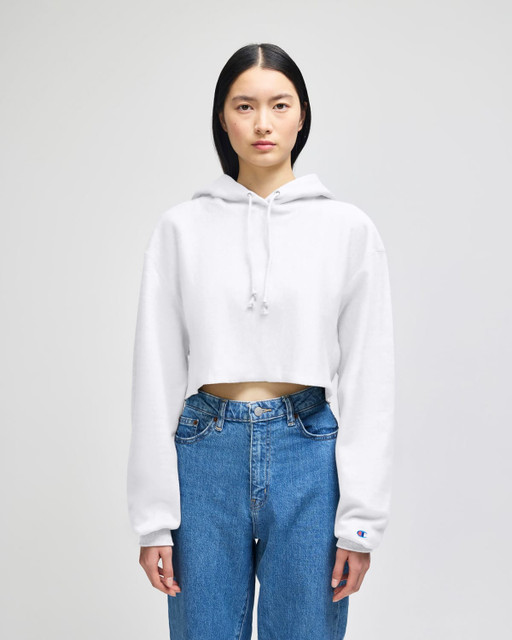 A white cropped hoodie with a hood, featuring long sleeves, paired with blue jeans, and includes a logo.