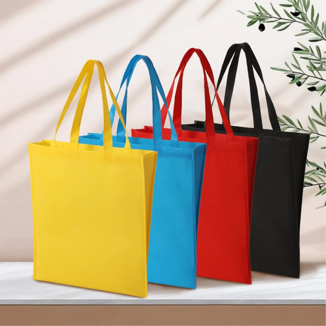 A set of four tote bags in yellow, blue, red, and black, featuring sturdy handles and a simple design.