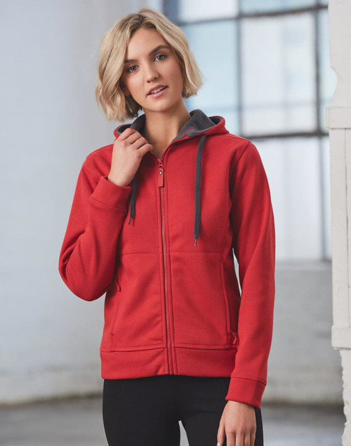 A red full zip fleece hoodie with a grey hood, featuring a logo, posed by a model in a bright interior setting.