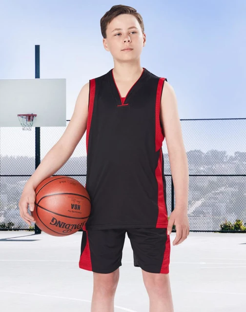 A young boy stands on a basketball court wearing black and red basketball shorts and a matching sleeveless top, holding a basketball.