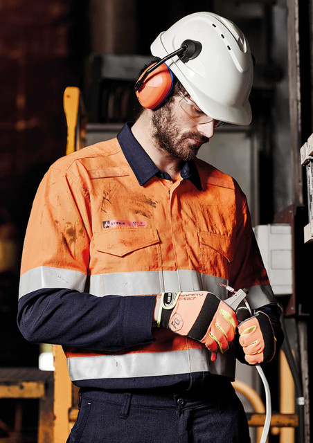 A man in a hi-vis orange and navy shirt with hoop taping, wearing safety earmuffs and a helmet.
