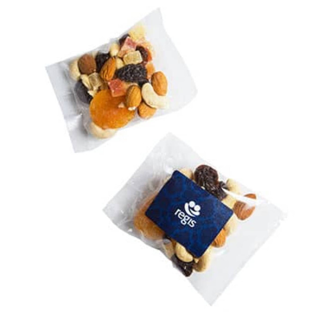 A transparent bag containing a mix of nuts, dried fruits, and a blue branded label. The contents have various colours including brown, yellow, and red.
