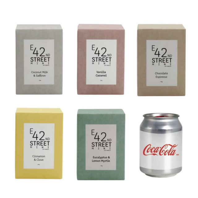 A set of six square candle boxes in various pastel colours: coconut milk and saffron, vanilla caramel, chocolate espresso, cinnamon and clove, eucalyptus and lemon myrtle. A Coca-Cola can is beside them.