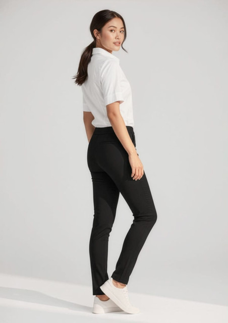 A woman wearing black stretch pants paired with a white shirt and white shoes, featuring a simple background.