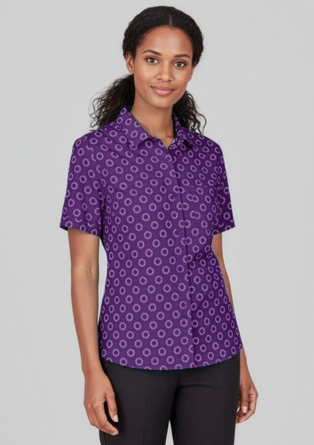 A short sleeve button-up shirt in purple with a daisy print pattern, featuring a branding logo.