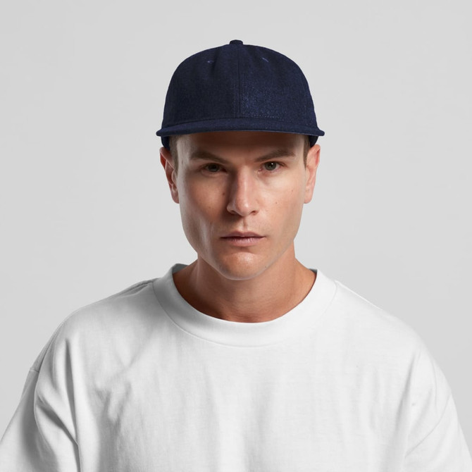 A wool cap in navy blue, featuring a solid design and a logo, worn by a model in a white shirt.