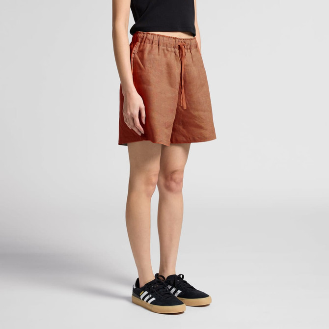 Linen shorts in a rust orange colour, featuring an elastic waistband and drawstring, styled with black sneakers.