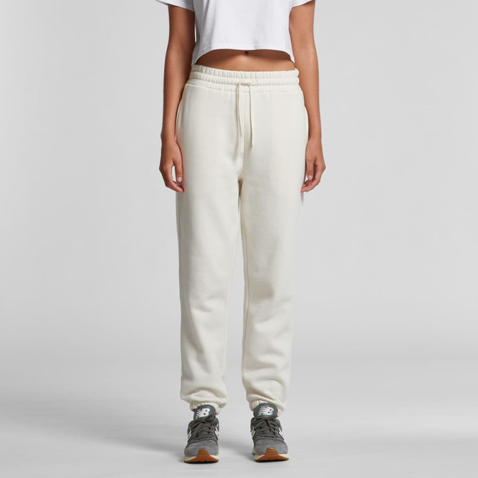 A pair of cream track pants with a drawstring waist and a logo, styled with a cropped top and grey sneakers.