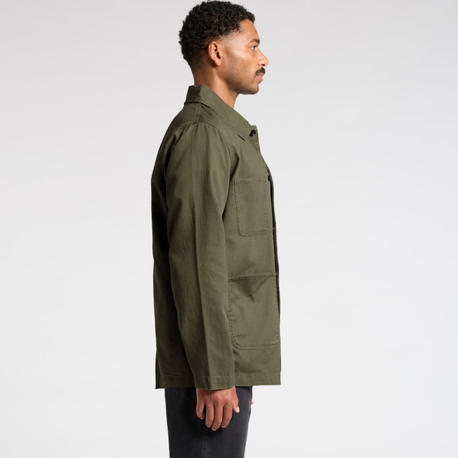 A man wearing an olive green canvas chore jacket, viewed from the side, with a simple design and a logo present.