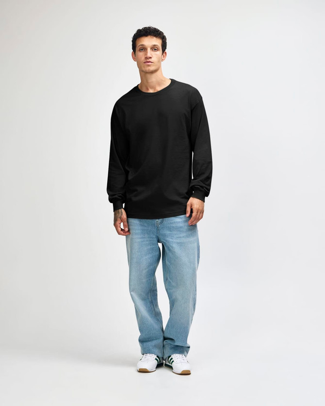 A model wearing a black heavyweight cotton unisex long sleeve T-shirt, paired with green cargo pants and white sneakers.