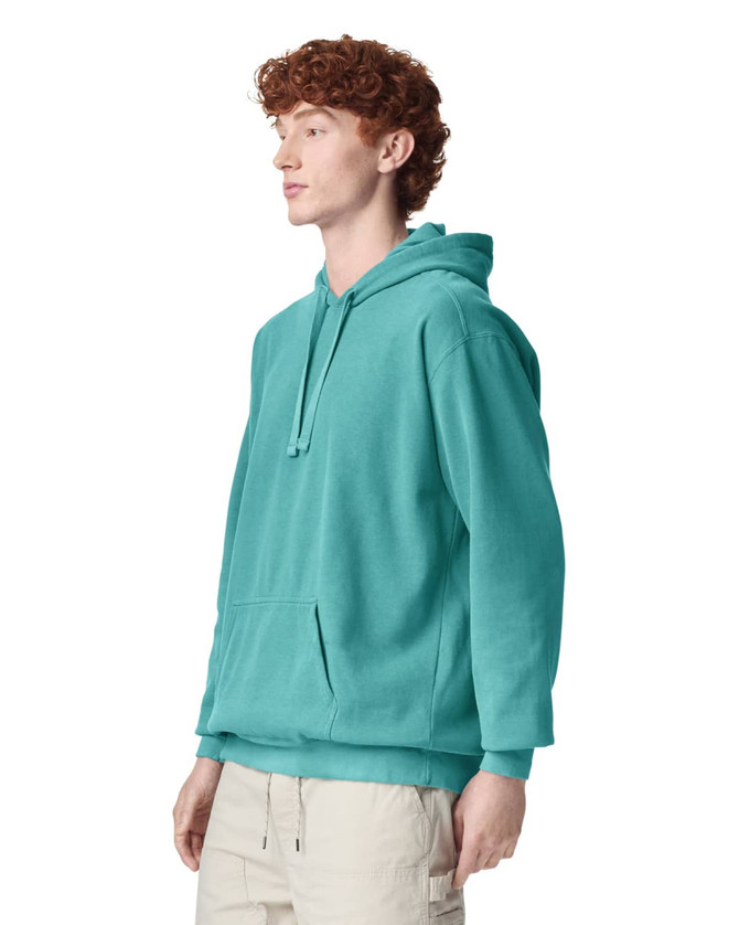 A turquoise adult hooded sweatshirt with a front pocket and a loose fit. The model stands facing to the side.