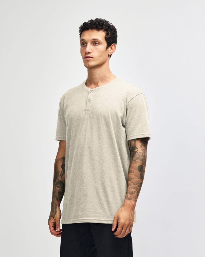 A unisex henley T-shirt in beige, featuring a round neckline and short sleeves, displayed on a model.
