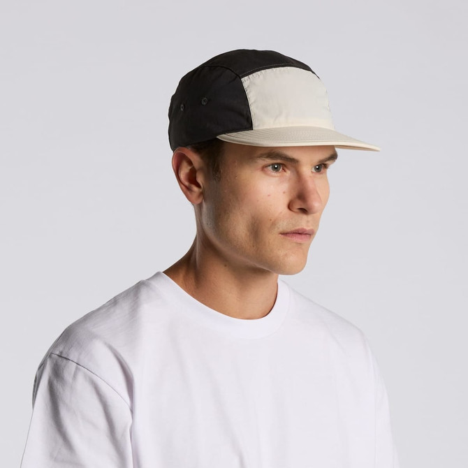 A two-tone nylon cap in black and cream, featuring a logo, worn by a model with a neutral expression.