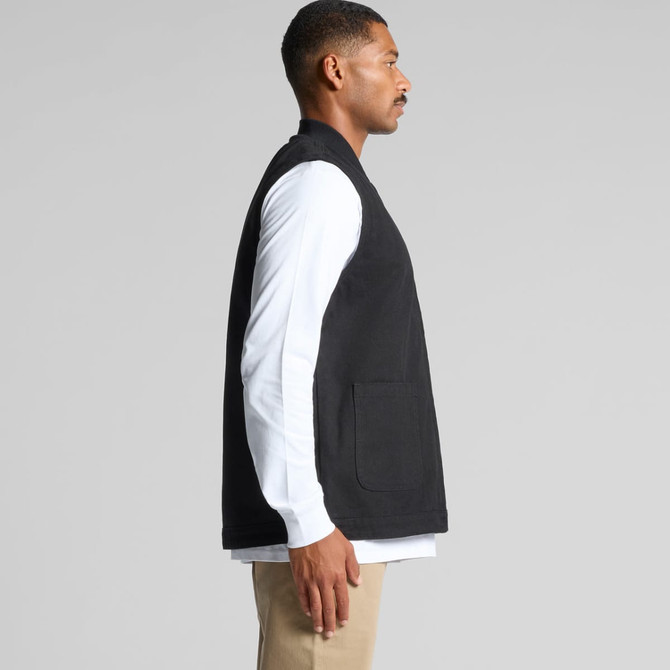 A black canvas vest is displayed, featuring a pocket and a clean, minimalist design. The model is wearing a white long-sleeve shirt underneath.