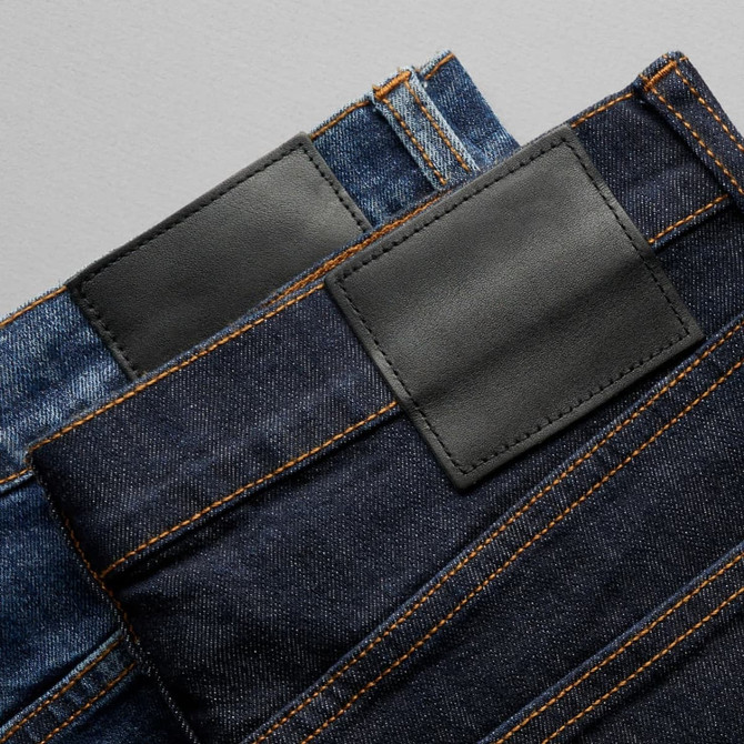 Two pairs of jeans in blue and dark denim, featuring leather patches and contrasting stitching.