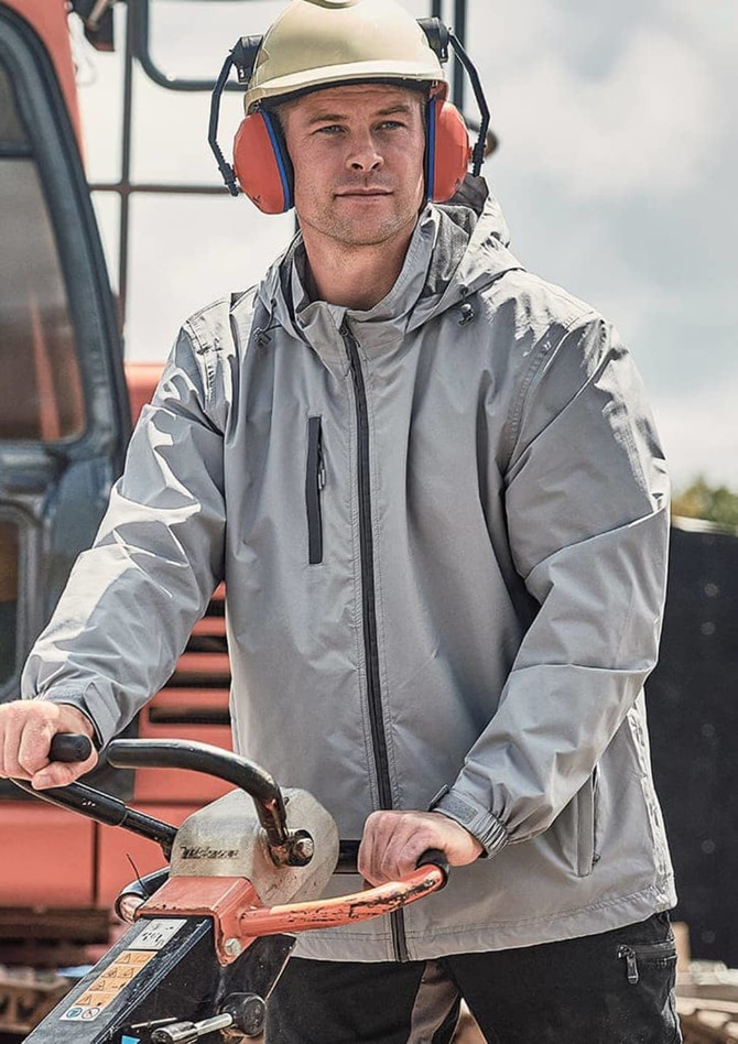 A man wearing a light grey unisex packable rain jacket, with a helmet and ear protection, operating machinery outdoors.