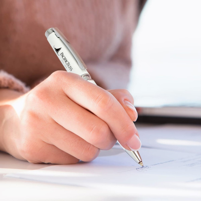A metal pen in silver being held while writing on paper. The pen features a logo.