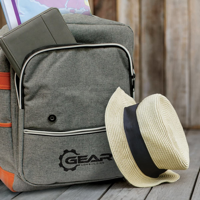 A grey Nirvana Backpack with an orange stripe, a notebook, a map, and a straw hat resting beside it.