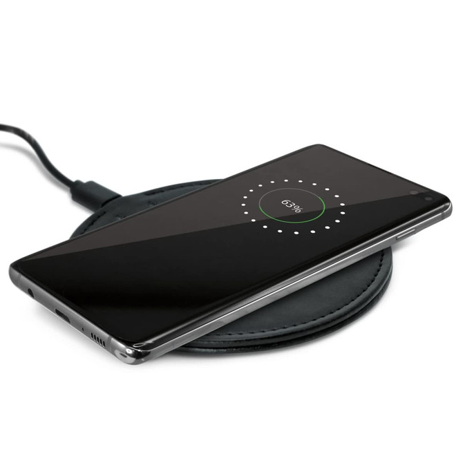 A wireless charger with a smartphone placed on top, displaying a charging indicator on the screen.