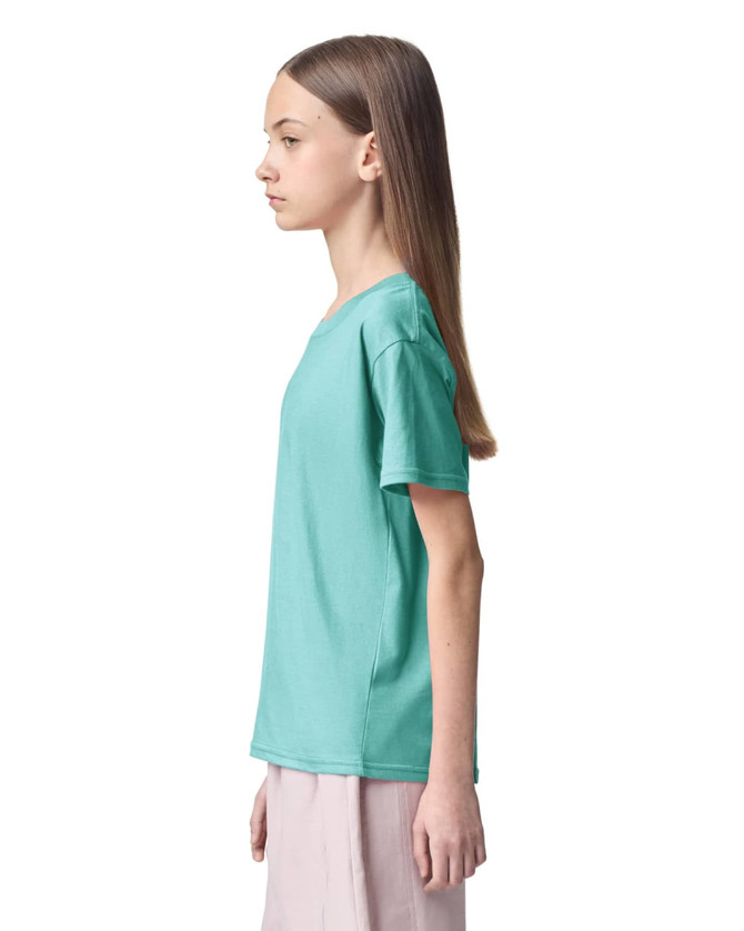 A turquoise youth t-shirt is displayed on a model standing in profile. The shirt features short sleeves and has a logo.