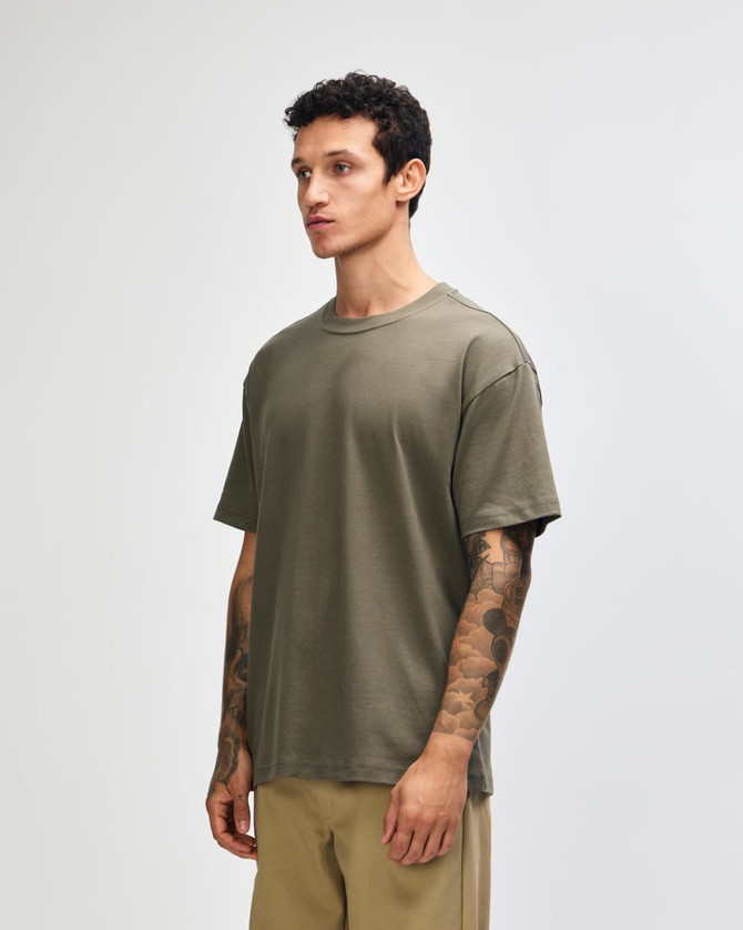 A green American Apparel super heavyweight t-shirt displayed on a model standing upright, featuring a round neckline.