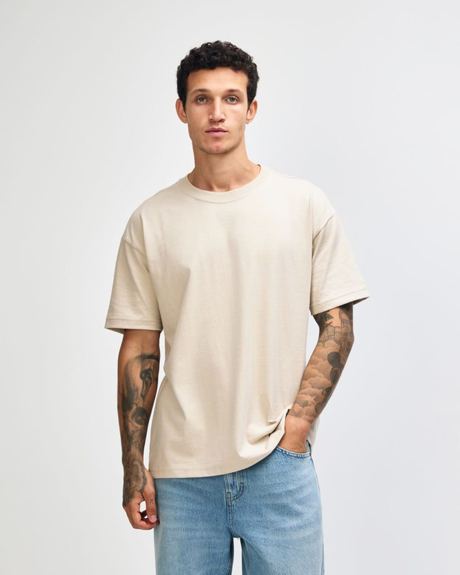 A light beige American Apparel Super Heavyweight T-Shirt on a model, featuring a relaxed fit and crew neck design.