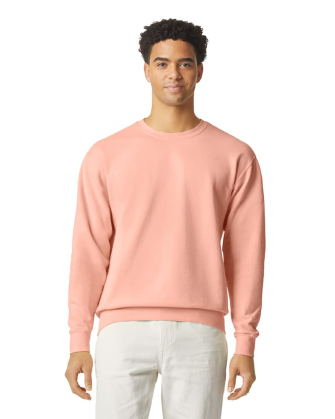 A lightweight crewneck sweatshirt in pastel pink featuring a logo. The model is wearing light-coloured pants.