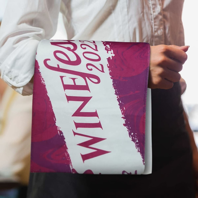 A bar towel with a vibrant design in shades of purple and white, featuring a logo.
