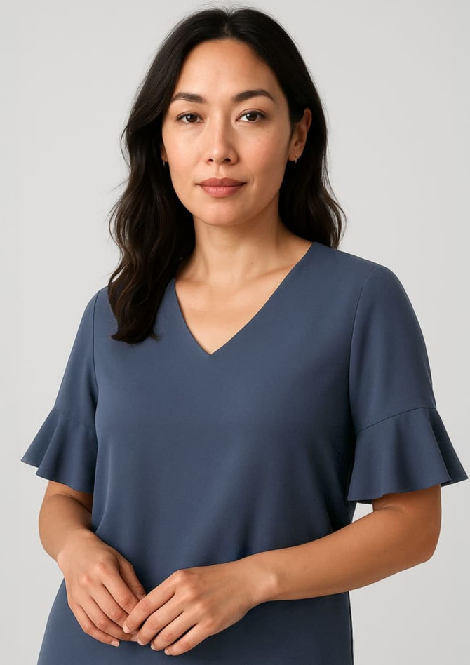 A woman wearing a dark blue blouse with fluted sleeves and a v-neckline, featuring a simple design and soft fabric.