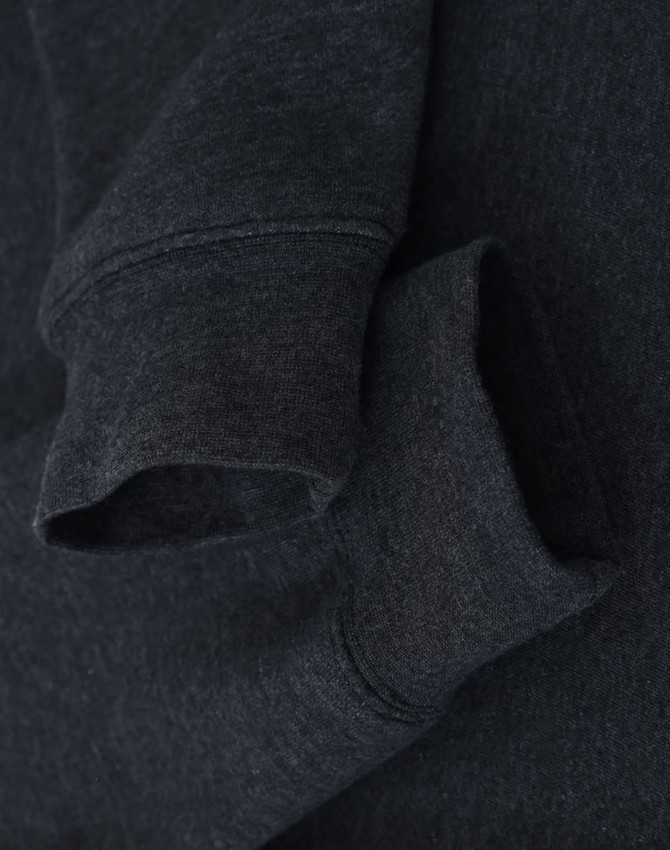 A dark grey crewneck sweatshirt featuring a soft fleece texture and rolled cuffs. It has a logo near the neckline.