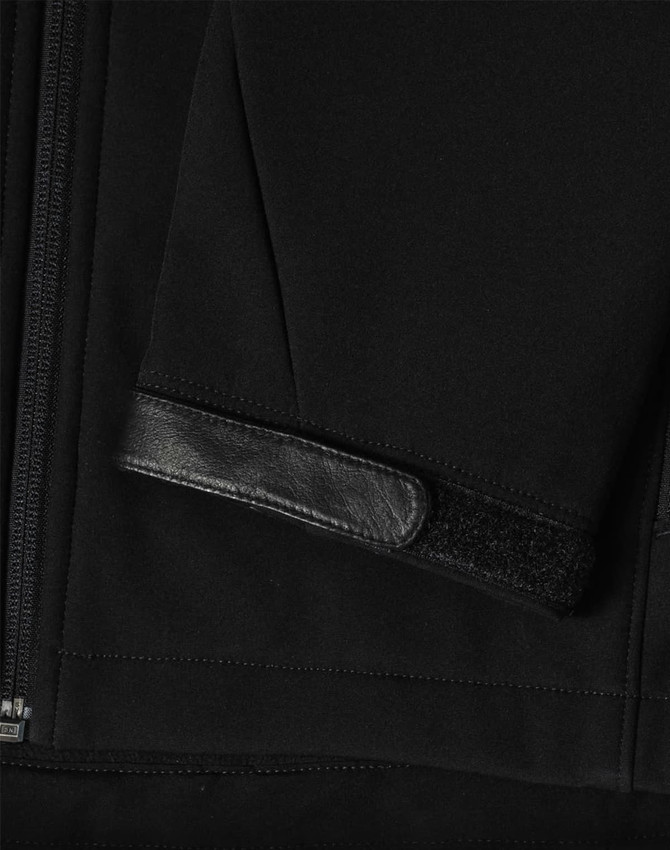 A black softshell jacket featuring a zippered front and a textured patch on the sleeve. It has a logo.
