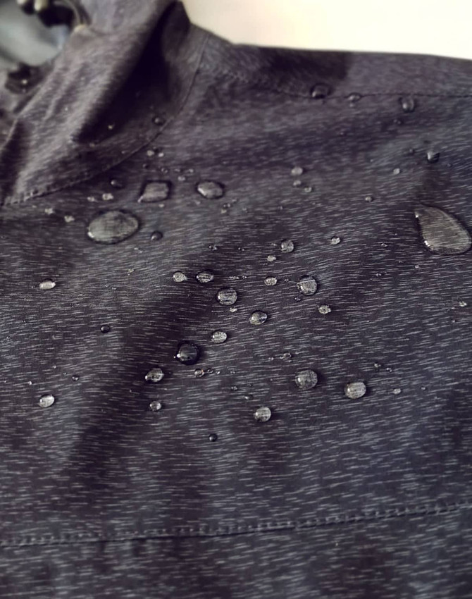 A close-up of a black waterproof performance jacket featuring droplets of water on the surface.