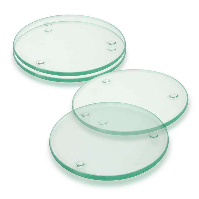 A set of four round glass coasters in a light green hue, featuring raised dots for grip.