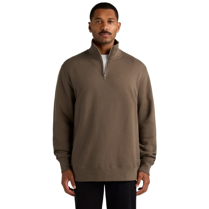 A man wearing a brown half zip crew jumper. The sweater features a zip at the collar and has an additional logo.