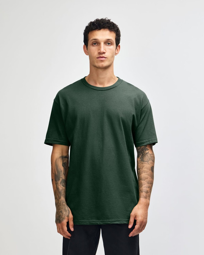 A unisex heavyweight cotton T-shirt in a dark green colour, displayed on a model with curly hair.