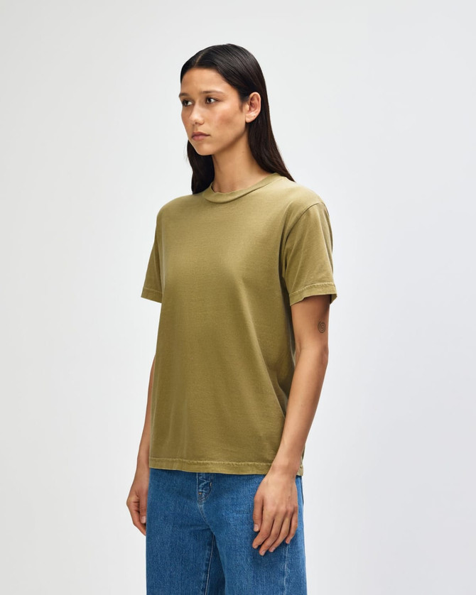 A heavyweight cotton unisex T-shirt in olive green, displayed on a model with curly hair. It features a simple design and branding.