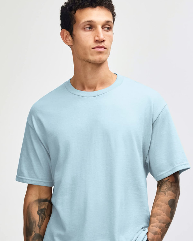 A light blue heavyweight cotton unisex T-shirt displayed on a model with short curly hair. It has a logo.