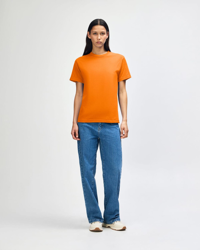 A heavyweight unisex t-shirt in bright orange, paired with light blue baggy jeans, modeled by a young person.