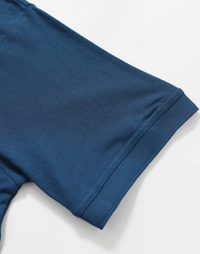 A close-up of a blue polo shirt sleeve with a smooth texture and cuff detail, featuring a logo.