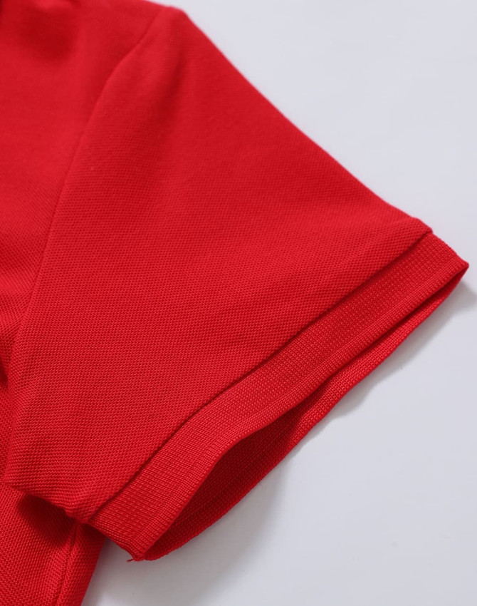 A red polo shirt featuring a textured fabric and a folded sleeve detail. It has a logo on the garment.