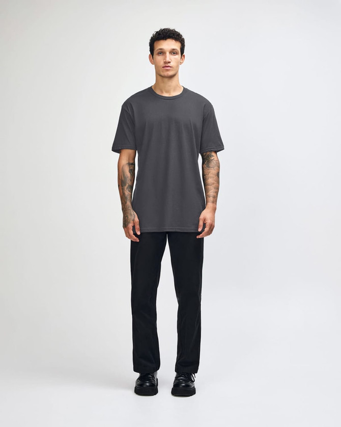 A unisex fine jersey short sleeve t-shirt in black, worn with beige pants and blue sneakers, with a logo visible.