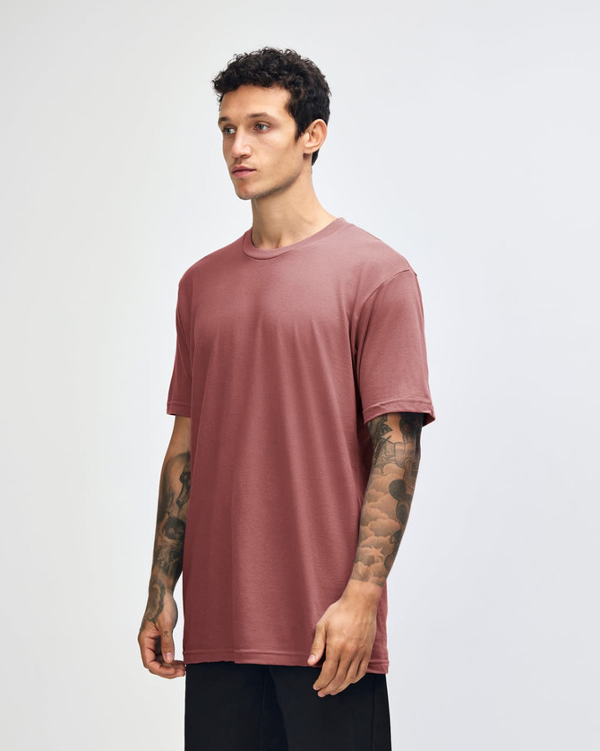 A side view of a woman wearing a rose pink unisex short sleeve T-shirt. The shirt has a simple design and a logo.