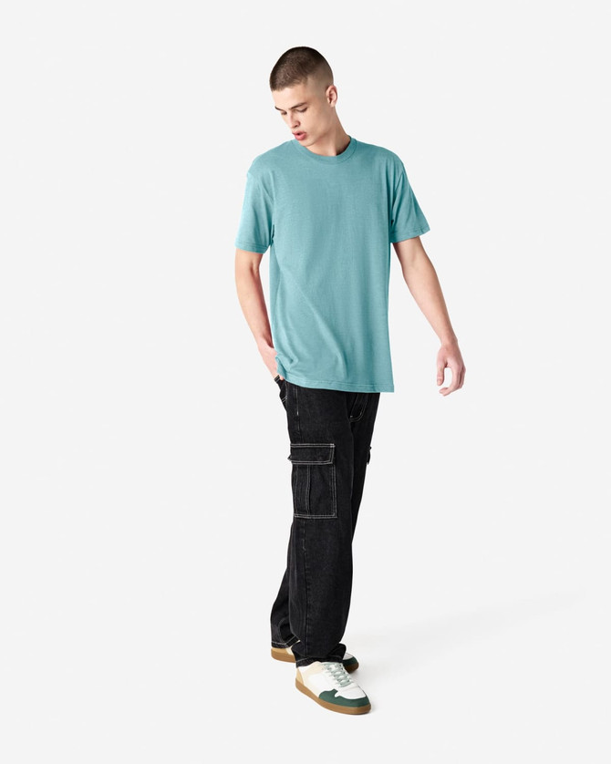 A unisex short sleeve t-shirt in a teal colour, paired with black cargo pants and casual shoes. The model has a relaxed pose.